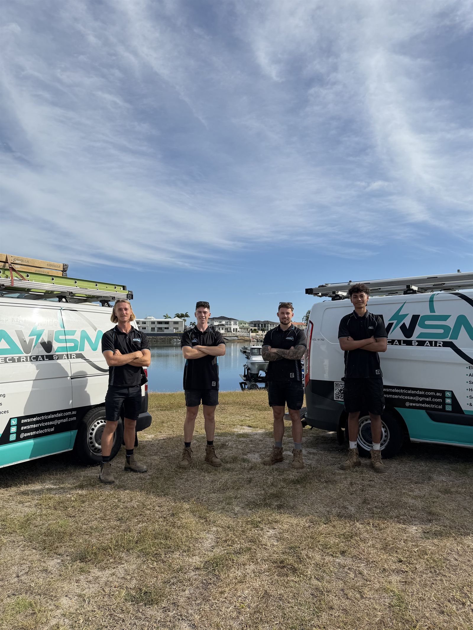 The AWSM Electrical & Air team — four sparkies standing in front of two branded AWSM vans in Moreton Bay